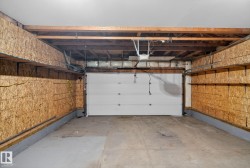 Spacious garage featuring a white paneled overhead door, exposed beam ceiling with mechanical systems, concrete flooring, and cork-faced side walls providing insulation and durability - 