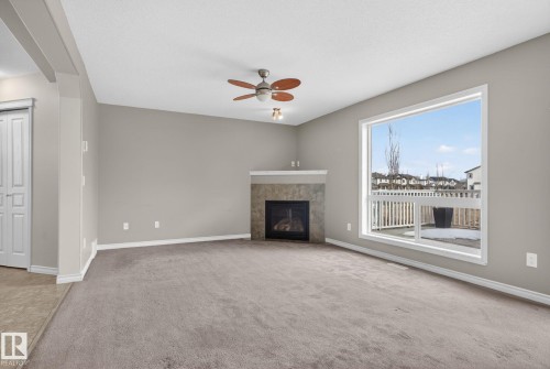 Spacious living area featuring a corner fireplace with stone-finish surround and mantel, a large picture window, and a ceiling fan with light fixture - 96 Dalquist Bay, Leduc, AB - Indoor Photo Showing Other Room With Fireplace