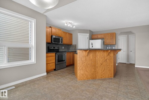 Spacious kitchen featuring wood-finish cabinetry, a large center island with wood-finish base, black stainless steel appliances including a slide-in range and microwave, dark countertops, and ceramic tile flooring throughout the open layout - 96 Dalquist Bay, Leduc, AB - Indoor Photo Showing Kitchen