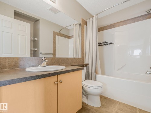 Bathroom featuring a neutral palette, a light-toned vanity with a dark countertop, an integrated sink, a chrome faucet, and a shower-over-tub combination with a tiled surround - 11844 21 Avenue Sw, Edmonton, AB - Indoor Photo Showing Bathroom