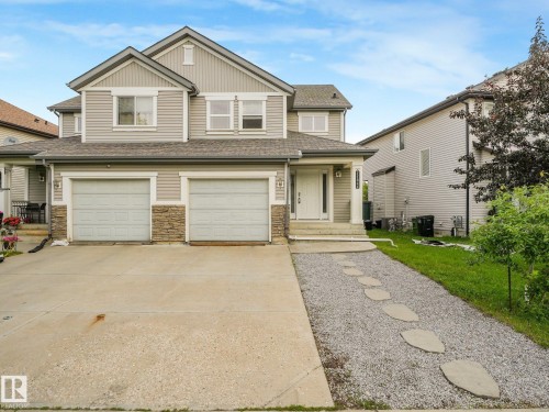 Welcoming two-car garage with neutral finish doors anchors this two-story home featuring crisp siding, stone accents, and a gabled roofline - 11844 21 Avenue Sw, Edmonton, AB - Outdoor With Facade