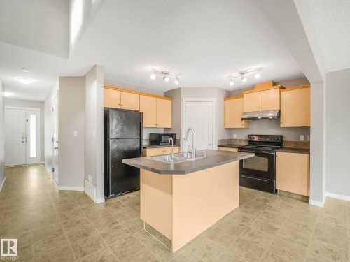 Spacious kitchen featuring light wood cabinetry, a large center island with stainless steel countertop, stainless steel appliances including a gas range and over-the-range microwave, black refrigerator, and a undermount sink - 11844 21 Avenue Sw, Edmonton, AB - Indoor Photo Showing Kitchen With Double Sink