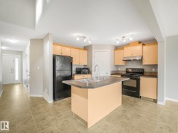 Spacious kitchen featuring light wood cabinetry, a large center island with stainless steel countertop, stainless steel appliances including a gas range and over-the-range microwave, black refrigerator, and a undermount sink - 