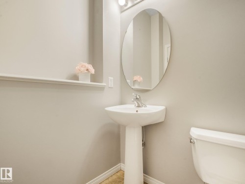 Pedestal sink with a chrome faucet, oval mirror, and wall-mounted vanity lighting - 11844 21 Avenue Sw, Edmonton, AB - Indoor Photo Showing Bathroom