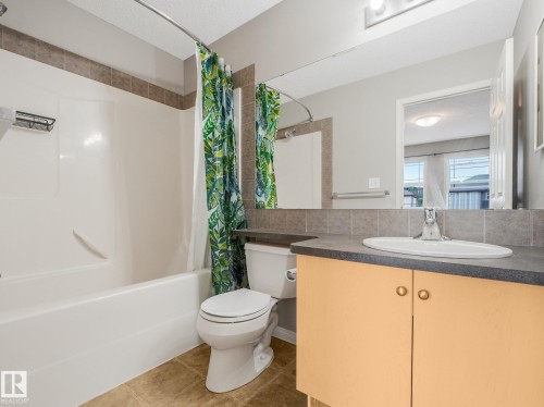 Bathroom featuring an integrated bathtub and shower with brown accent tile, a single vanity with a laminate countertop, and tan tile flooring - 11844 21 Avenue Sw, Edmonton, AB - Indoor Photo Showing Bathroom