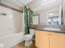 Bathroom featuring an integrated bathtub and shower with brown accent tile, a single vanity with a laminate countertop, and tan tile flooring - 