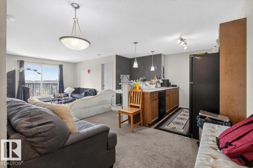 Open-concept living space featuring a sliding glass door, a kitchen island with pendant lighting, wood cabinetry, and a black appliance suite - #421 1180 Hyndman Rd Nw, Edmonton, AB - Indoor Photo Showing Living Room