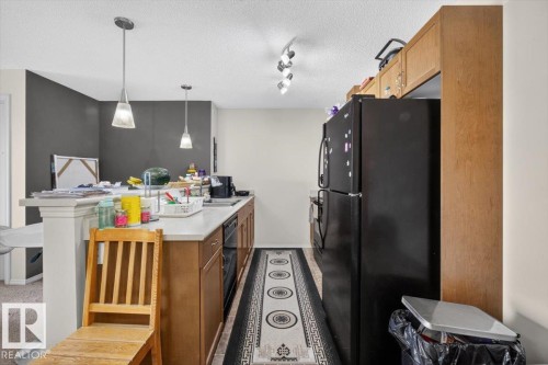Kitchen featuring wood-finish cabinetry, light-toned countertops, and a black appliance suite - #421 1180 Hyndman Rd Nw, Edmonton, AB - Indoor