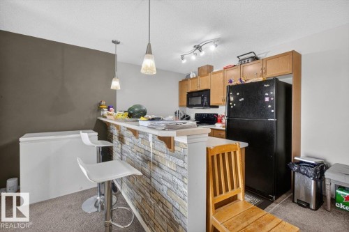 Kitchen area featuring a breakfast bar with a stone-look facade - #421 1180 Hyndman Rd Nw, Edmonton, AB - Indoor Photo Showing Kitchen