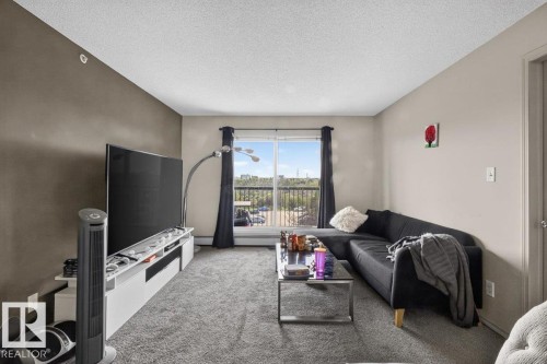 Living area featuring broadloom carpeting and a window with a balcony beyond - #421 1180 Hyndman Rd Nw, Edmonton, AB - Indoor