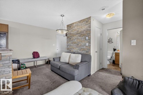 Living area featuring a textured accent wall, light grey wall paint, and grey carpet flooring - #421 1180 Hyndman Rd Nw, Edmonton, AB - Indoor