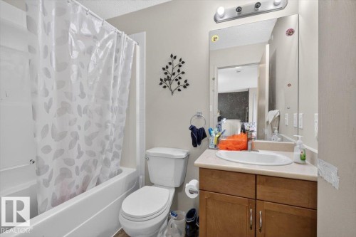 Full bathroom featuring a white porcelain toilet, bathtub with tile surround, and a wood-finish vanity with an integrated sink and light-toned countertop - #421 1180 Hyndman Rd Nw, Edmonton, AB - Indoor Photo Showing Bathroom