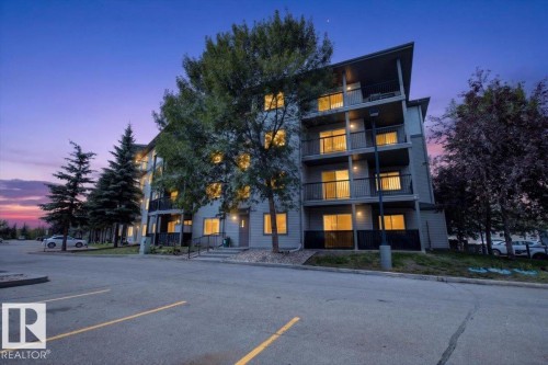 Modern multi-story building featuring a sloped roofline, balconies with black railings, and a light gray exterior finish - #421 1180 Hyndman Rd Nw, Edmonton, AB - Outdoor With Facade
