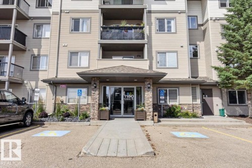 Multi-story residential building featuring a stone and siding exterior, covered entry, glass double doors, and a concrete walkway - #421 1180 Hyndman Rd Nw, Edmonton, AB - Outdoor With Facade