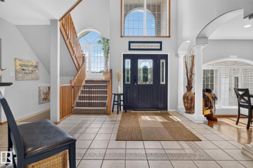 Two-story foyer featuring tile flooring, a dark paneled front door with decorative glass inserts, an arched transom window, a wooden staircase with carpeted treads, and an arched entryway with columns - 50336 Range Road 280, Rural Leduc County, AB - Indoor Photo Showing Other Room