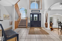 Two-story foyer featuring tile flooring, a dark paneled front door with decorative glass inserts, an arched transom window, a wooden staircase with carpeted treads, and an arched entryway with columns - 