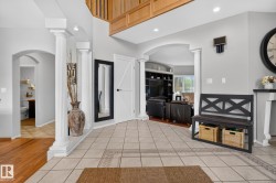 Entryway featuring tile flooring with decorative inlay, architectural columns, an arched doorway, and an upper-level wood-finish railing - 