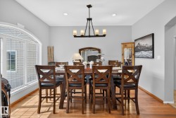 Spacious dining area featuring wood-finish flooring, a contemporary chandelier, recessed lighting, and a large arched window with grid detailing - 