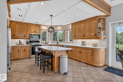 Kitchen featuring wood cabinetry, stainless steel appliances, a center island with seating, a coffered ceiling, and tiled flooring - 