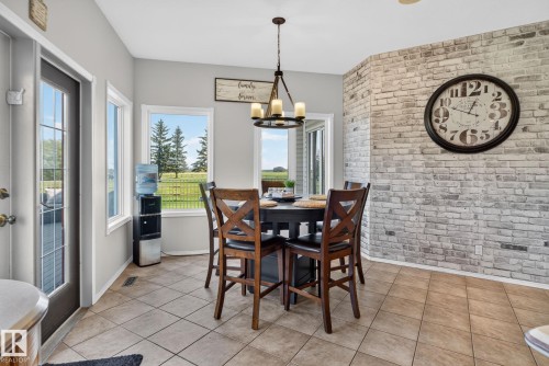 Dining area featuring a textured brick accent wall, tiled flooring, and a contemporary chandelier - 50336 Range Road 280, Rural Leduc County, AB - Indoor Photo Showing Dining Room