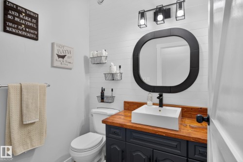 Modern bathroom featuring a striking rounded black-framed mirror, vessel sink with chrome faucet mounted on a warm wood-finish vanity, and black cabinetry with ample storage - 50336 Range Road 280, Rural Leduc County, AB - Indoor Photo Showing Bathroom