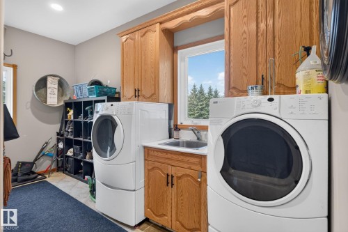 Dedicated laundry space featuring a utility sink, wood-finish cabinetry, and a window with outdoor scenery - 50336 Range Road 280, Rural Leduc County, AB - Indoor Photo Showing Laundry Room