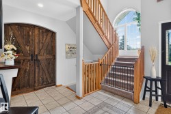 Foyer featuring a grand staircase with wood railings, an arched window, and barn doors with dark hardware - 