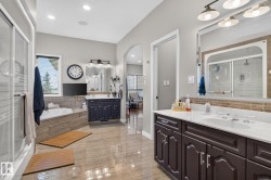 Spacious bathroom featuring a dual vanity with white countertops, a deep soaking tub, a separate glass-enclosed shower, and large format tile flooring - 