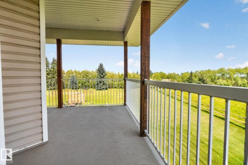 Expansive covered deck with composite decking, metal railings, and support columns overlooking manicured grounds and tree-lined landscape - 50336 Range Road 280, Rural Leduc County, AB - Outdoor With Exterior