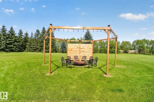 Expansive green lawn with a wooden pergola featuring string lighting and a built-in fire pit - 50336 Range Road 280, Rural Leduc County, AB - Outdoor
