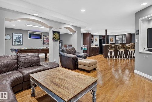 Open-concept living space featuring rich wood-finish flooring throughout, a leather sectional sofa, and a substantial wood dining table - 50336 Range Road 280, Rural Leduc County, AB - Indoor