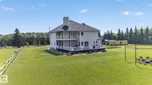 Expansive green lawn surrounds this property featuring a two-story exterior with an upper-level balcony, lower-level deck, and multiple exterior doors - 50336 Range Road 280, Rural Leduc County, AB - Outdoor
