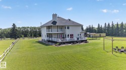 Expansive green lawn surrounds this property featuring a two-story exterior with an upper-level balcony, lower-level deck, and multiple exterior doors - 