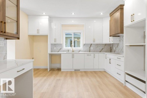 Bright kitchen featuring white cabinetry with gold-tone hardware, a light wood-finish floor, and a white countertop with a matching backsplash - 10323 79 Street Nw, Edmonton, AB - Indoor Photo Showing Kitchen
