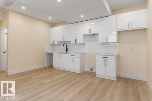 Bright, open kitchen space featuring white cabinetry throughout, stainless steel sink with matte black faucet, recessed ceiling lighting, and wood-finish flooring - 10323 79 Street Nw, Edmonton, AB - Indoor Photo Showing Kitchen