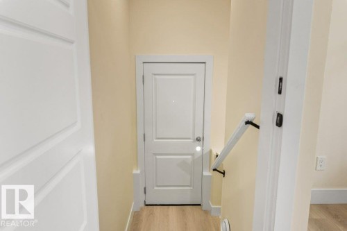 Secondary Suite Entrance - Hallway featuring a white paneled door, light wood-finish flooring, light beige wall paint, white baseboards, and a white handrail with dark brackets - 10323 79 Street Nw, Edmonton, AB - Indoor Photo Showing Other Room