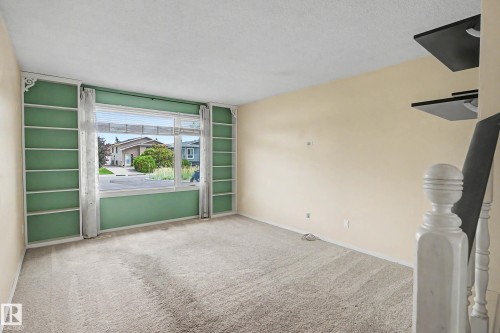 Carpeted living space featuring a large picture window, integrated built-in shelving, and neutral wall tones - 10032 173 Avenue Nw, Edmonton, AB - Indoor Photo Showing Other Room