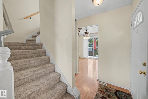 Entryway featuring a carpeted staircase with wood handrail, light wood-finish flooring, a white front door with an arched window, and an overhead flush-mount light fixture - 10032 173 Avenue Nw, Edmonton, AB - Indoor Photo Showing Other Room