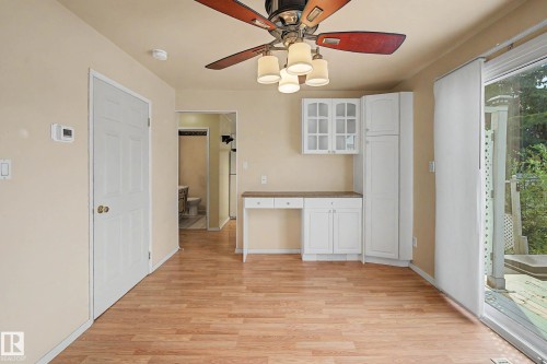Bright, open kitchen and dining area featuring wood-finish flooring throughout, white cabinetry with glass-front upper storage, built-in countertop workspace, and a ceiling fan with integrated lighting - 10032 173 Avenue Nw, Edmonton, AB - Indoor Photo Showing Other Room