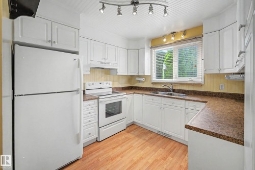 Kitchen featuring white cabinetry, built-in appliances, wood-finish flooring, and track lighting - 10032 173 Avenue Nw, Edmonton, AB - Indoor Photo Showing Kitchen With Double Sink