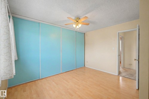 Room featuring wood-finish flooring, full-wall sliding closet doors with blue panels, a ceiling fan with integrated lighting, and neutral wall paint - 10032 173 Avenue Nw, Edmonton, AB - Indoor Photo Showing Other Room