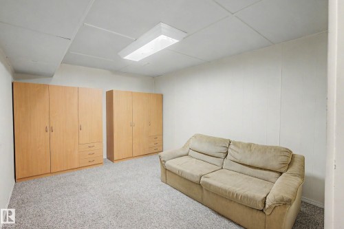 Carpeted room featuring two wood-finish wardrobe units with multiple doors and drawers, white paneled walls, and a recessed ceiling with a fluorescent light fixture - 10032 173 Avenue Nw, Edmonton, AB - Indoor
