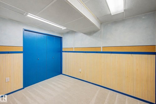 Room featuring light-colored carpet flooring, blue bi-fold closet doors, and wood-panel wainscoting - 10032 173 Avenue Nw, Edmonton, AB - Indoor Photo Showing Other Room