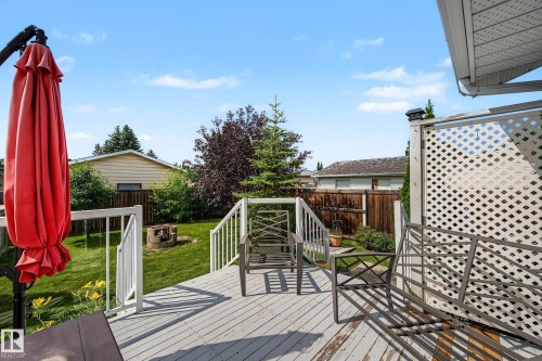 Spacious outdoor deck with white railings and lattice screening, overlooking a green lawn with mature trees and a built-in fire pit - 10032 173 Avenue Nw, Edmonton, AB - Outdoor With Deck Patio Veranda