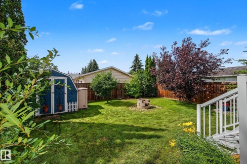 Expansive green lawn featuring a built-in fire pit, mature trees, and a storage shed with a white picket fence detail - 10032 173 Avenue Nw, Edmonton, AB - Outdoor