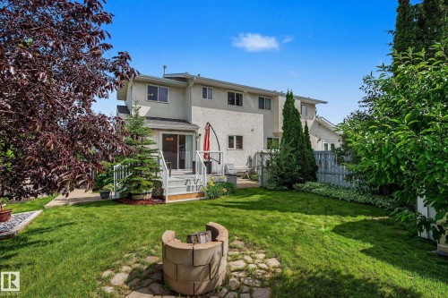 Expansive green lawn with a stone fire pit, bordered by mature trees and shrubs - 10032 173 Avenue Nw, Edmonton, AB - Outdoor