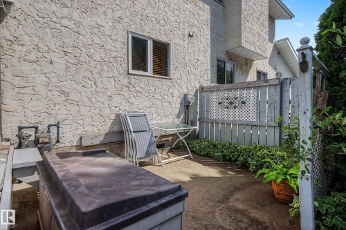 Outdoor living space featuring a concrete patio with built-in seating bench, metal railing with decorative lattice panel, and mature landscaping including potted plants and climbing ivy - 10032 173 Avenue Nw, Edmonton, AB - Outdoor