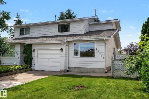 Two-story duplex featuring white siding, an attached garage, a paved driveway, and a front lawn with mature landscaping - 10032 173 Avenue Nw, Edmonton, AB - Outdoor With Exterior