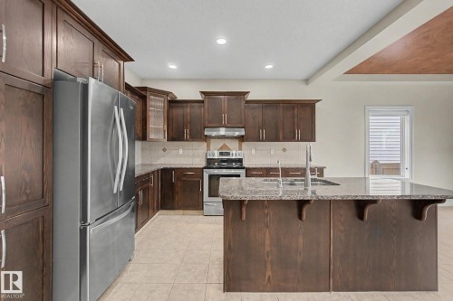 Kitchen featuring wood-finish cabinetry, stainless steel appliances, a center island with sink and integrated dishwasher, light-toned tile flooring, and recessed lighting - 6016 10 Avenue Sw, Edmonton, AB - Indoor Photo Showing Kitchen With Double Sink With Upgraded Kitchen