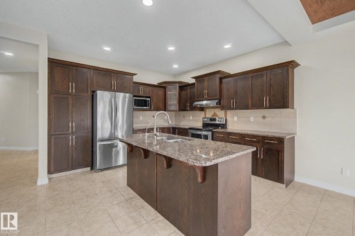 Spacious kitchen featuring an island with a sink, stainless steel appliances, extensive dark wood cabinetry, a tiled backsplash, and recessed lighting - 6016 10 Avenue Sw, Edmonton, AB - Indoor Photo Showing Kitchen With Double Sink With Upgraded Kitchen